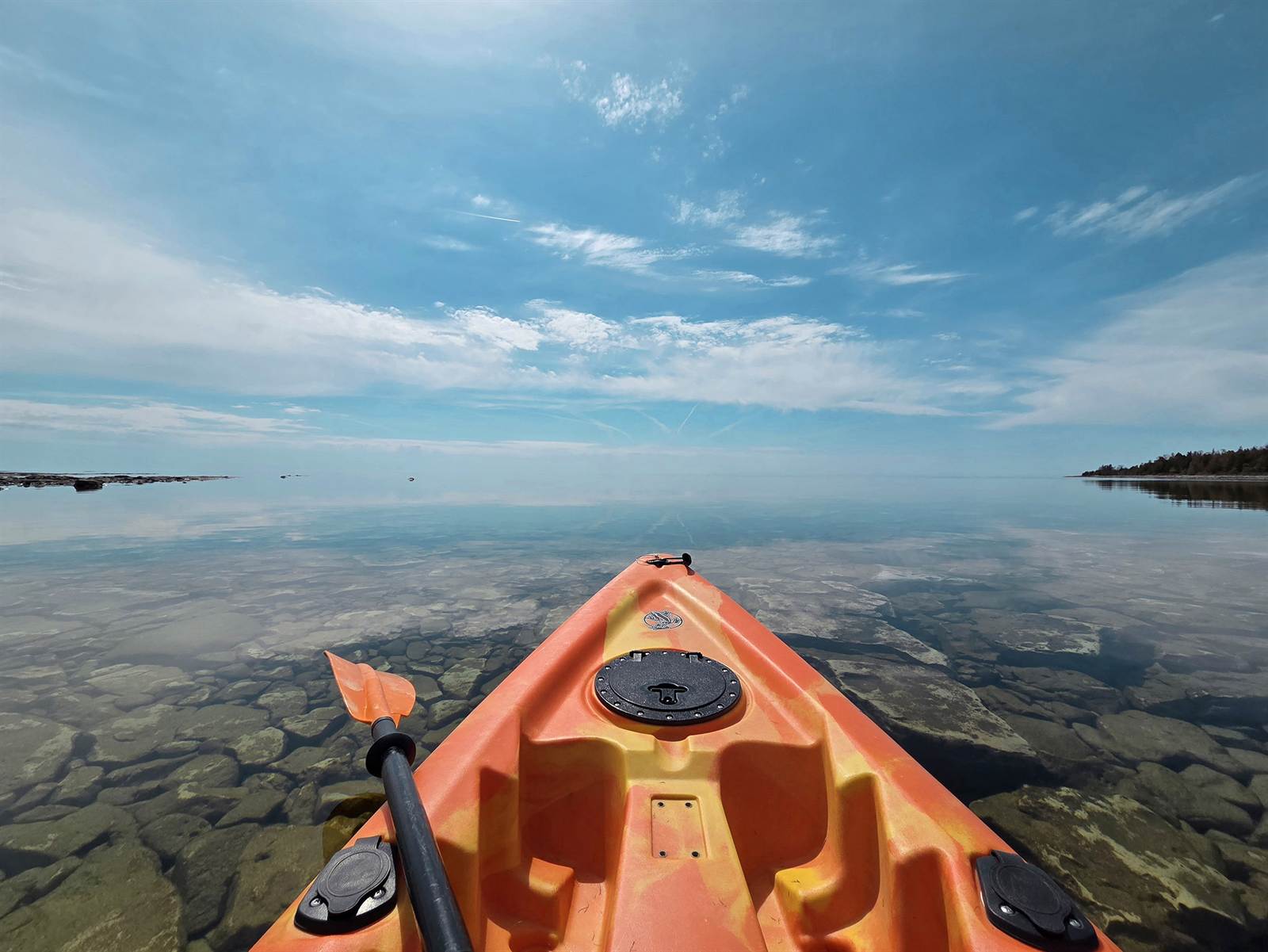 Kayak bow on clear turquoise water over cobblestones