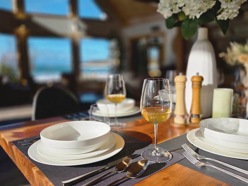 Close-up of white plates and bowls, wine glass, pepper mills and hydrangeas on a wood dining table
