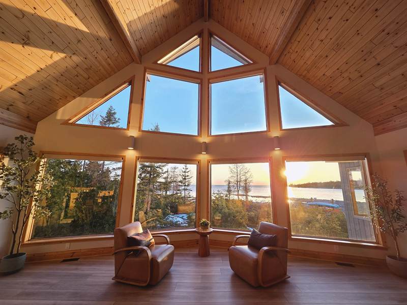 Vaulted window wall at sunset with the sun low over the bay, two leather armchairs silhouetted
