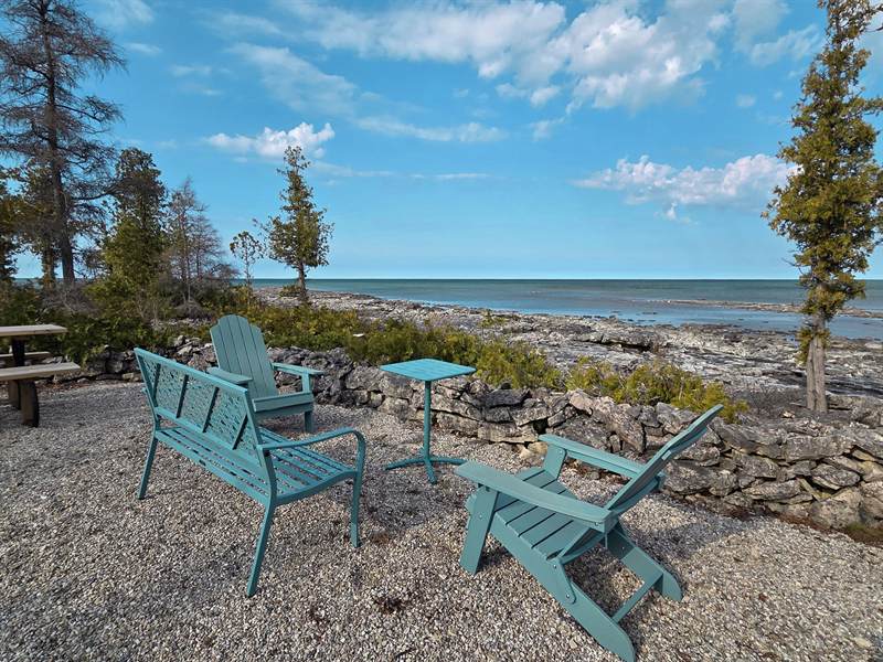 Teal Adirondack chairs, bench and side table on gravel at the water's edge by a low stone wall