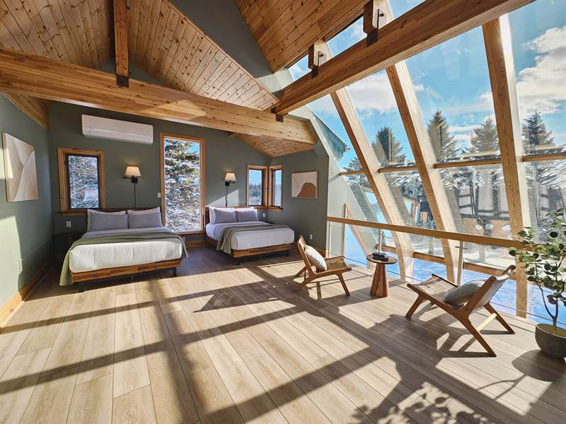 Loft bedroom with two beds, green walls, timber beams and angled glass wall showing snowy trees